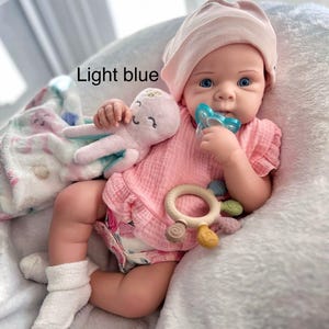May include: A baby doll in a pink outfit, hat, and socks, with a pacifier and a plush octopus toy. The doll is on a white blanket. The image includes the text "Light blue".