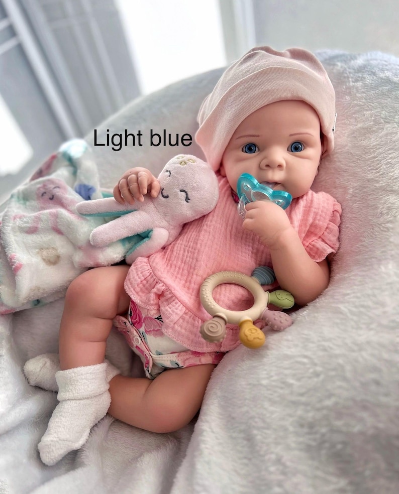 May include: A baby doll in a pink outfit, hat, and socks, with a pacifier and a plush octopus toy. The doll is on a white blanket. The image includes the text "Light blue".