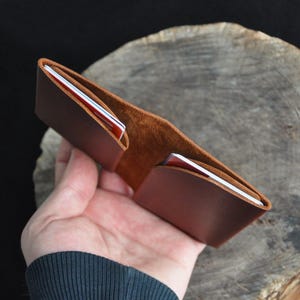 May include: A brown leather wallet, open to display card slots. The wallet is made of textured leather, with a lighter brown interior. Several cards are visible in the slots. The wallet is new and appears to be unused.