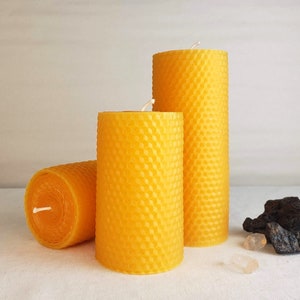 Puede incluir: Tres velas de cera de abeja amarilla con un patrón de panal. Las velas son de diferentes tamaños y están dispuestas en una fila sobre una superficie blanca.