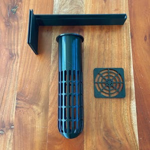 Può includere: Tre pezzi di plastica nera per un sistema idroponico stampato in 3D. I pezzi includono un cilindro verticale con un motivo a griglia, un quadrato con un motivo circolare e una barra orizzontale.