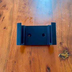 Op de afbeelding: Zwarte plastic wandbeugel met twee gaten.