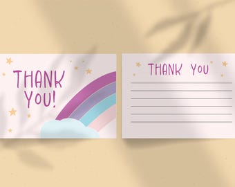 May include: Two-part stationery set featuring a thank you card with a rainbow and cloud design, and a lined card for writing. The words "THANK YOU!" are in purple, with gold star accents. The stationery is on a light pink background.