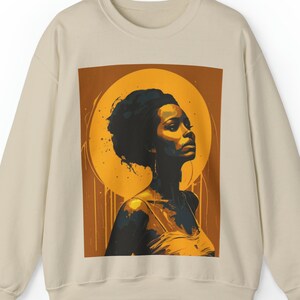 Könnte beinhalten: Ein beiger Pullover mit einem grafischen Druck einer Frau mit dunklen Haaren vor einem gelben Hintergrund. Die Frau blickt nach rechts und hat einen ernsten Ausdruck.