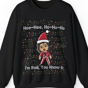 Może przedstawiać: Czarny świąteczny sweter z kreskówkową postacią Michaela Jacksona w czapce Świętego Mikołaja i czerwonym stroju. Sweter ma świąteczny wzór z zielonymi choinkami, czerwonymi i złotymi gwiazdami oraz tekstem "Hee-Hee, Ho-Ho-Ho" i "I'm Bad, You Know It."