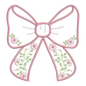 Puede incluir: Un lazo rosa con bordado floral blanco. El lazo tiene un bucle central y dos colas largas con diseños florales.