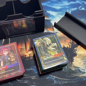 May include: A black plastic card storage box with two compartments, a separate black rectangular tray, and two stacks of trading cards. One stack features a character card labeled Dark Child, and the other features a card labeled Wuju Bladesman.