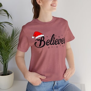 May include: A maroon t-shirt with a black graphic of a Santa hat and the word "Believer" with snowflakes.