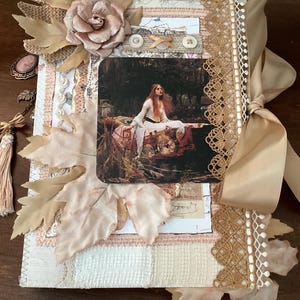 Op de afbeelding: Een handgemaakt dagboek met een collage-omslag. Het heeft een vintage schilderij, stoffen bladeren en een grote roos. Het dagboek is gebonden met een bruin lint en versierd met kant en decoratieve elementen in beige, roze en crèmetinten.