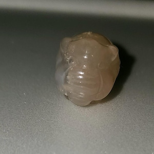 Peut inclure: Une petite perle ronde, blanche, opaque, sculptée avec un motif détaillé.