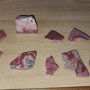 May include: A collection of ten pink and white patterned mineral stones. The stones are various shapes and sizes, and have a natural, rough texture.