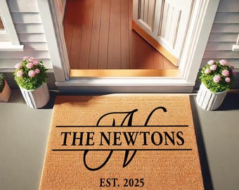 May include: A rectangular doormat with the text "THE NEWTONS" and "EST. 2025" in black. The mat has a monogram design with the letter "N". The mat is tan and sits in front of a white door.