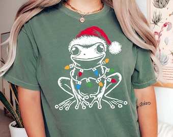 May include: A green t-shirt with a white frog wearing a red Santa hat and Christmas lights around its neck.