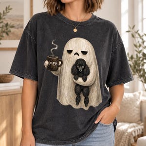 Könnte beinhalten: Ein anthrazitfarbenes, mineralgewaschenes T-Shirt mit einer Grafik eines beigen Geistes, der eine braune Kaffeetasse mit der Aufschrift MEH und einen kleinen schwarzen Pudel hält. Der Geist schaut traurig und Dampf steigt aus der Tasse auf.