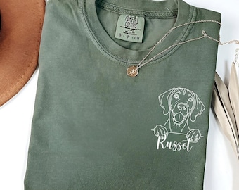 May include: A green t-shirt with a white outline of a dog's head peeking over the top and the name "Russet" written below.