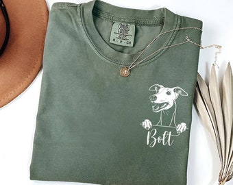 May include: A green t-shirt with a white illustration of a dog peeking over the top. The dog's name, "Bolt", is printed below the illustration.