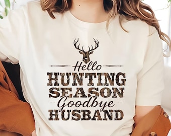 May include: White t-shirt with a brown camouflage print design featuring a deer head silhouette and the text "Hello Hunting Season Goodbye Husband".