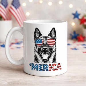 May include: White ceramic mug featuring a black and white illustration of a dog wearing sunglasses with the American flag design. The word "'MERICA" is printed below the dog in red, white, and blue.
