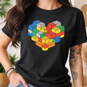 Op de afbeelding: Zwart t-shirt met een hartvormig ontwerp gemaakt van speelgoedbouwstenen. Het hart is samengesteld uit blauwe, groene, rode, gele en oranje blokken. Het t-shirt heeft een ronde hals.
