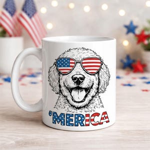 May include: White ceramic mug featuring a smiling dog wearing sunglasses with the American flag design. The word "'MERICA" is printed in red, white, and blue letters below the dog's face. Patriotic theme.