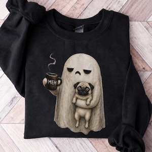 May include: A black crewneck sweatshirt featuring a graphic of a beige ghost with a sad expression holding a steaming dark mug labeled MEH and carrying a small tan pug dog. The design is centered on the front of the long-sleeved pullover garment.