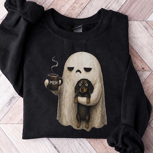 May include: A black crewneck sweatshirt featuring a graphic of a white ghost holding a brown mug with the text MEH and a small black and tan dachshund dog. The ghost has a neutral expression, and a thin wisp of steam rises from the mug.