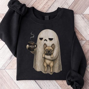 May include: A black long-sleeved sweatshirt featuring a graphic illustration of a beige ghost holding a dark mug with the text MEH printed on it. The ghost is also holding a tan French bulldog. The sweatshirt has a crew neckline and ribbed cuffs.