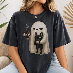 Op de afbeelding: Een antracietgrijs t-shirt met korte mouwen en een afbeelding van een witte geest die een bruine mok met de tekst MEH vasthoudt, samen met een zwarte Franse bulldog. De geest kijkt verveeld en het ontwerp staat centraal op het kledingstuk.