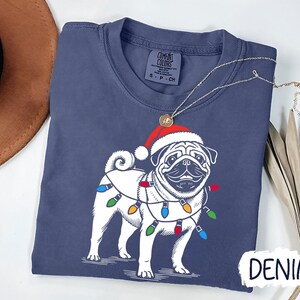 May include: A navy blue t-shirt with a white pug wearing a Santa hat and Christmas lights. The text "DENIM" is visible in the bottom right corner of the image.