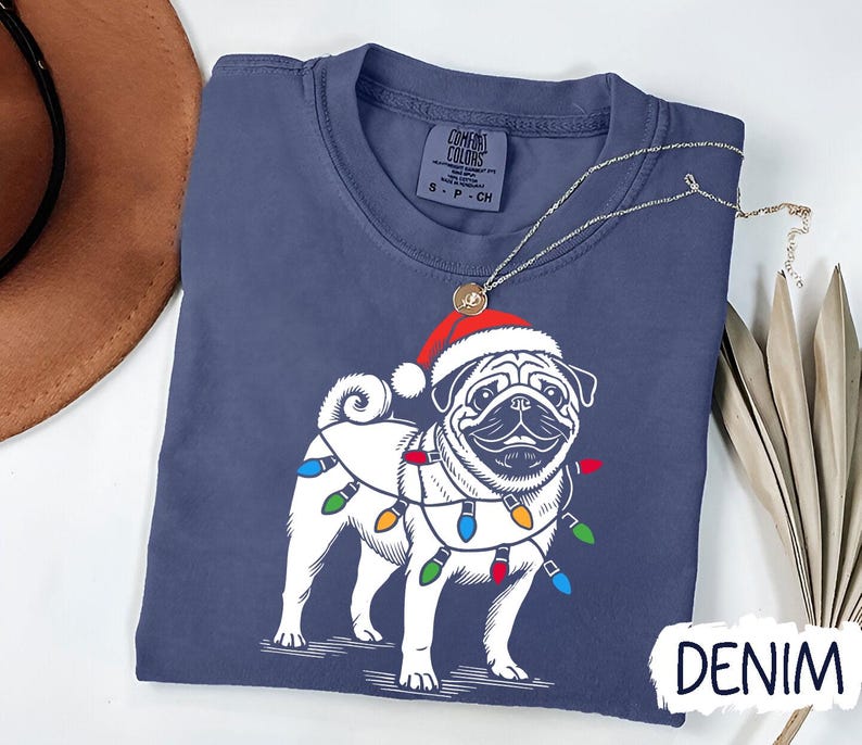 May include: A navy blue t-shirt with a white pug wearing a Santa hat and Christmas lights. The text "DENIM" is visible in the bottom right corner of the image.