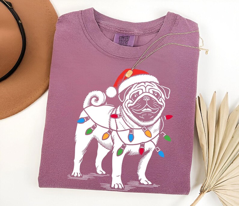 May include: A purple t-shirt with a white pug wearing a Santa hat and Christmas lights. The shirt has the text "Comfort Colors" on the tag.