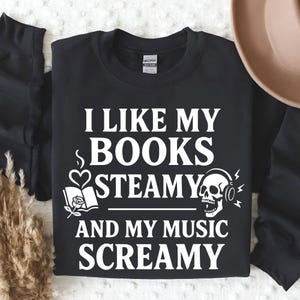 May include: Black sweatshirt with white text: "I LIKE MY BOOKS STEAMY AND MY MUSIC SCREAMY." Graphic includes a book, heart, and skull with headphones. A cozy apparel item for book and music lovers.