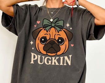 Könnte beinhalten: Dunkelgraues T-Shirt mit einem kürbisförmigen Mops-Design und einer grünen Schleife. Das Design enthält das Wort "PUGKIN" in einer Serifenschrift sowie Herzen und Sterne. Das Shirt hat eine lockere Passform.