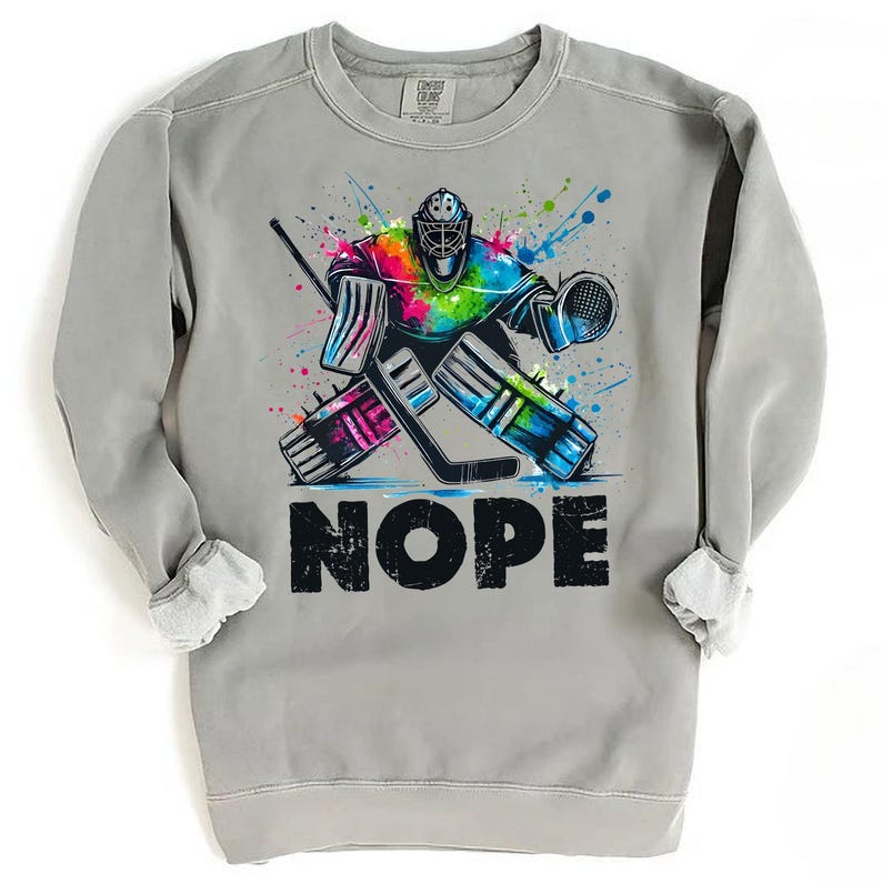 May include: A gray sweatshirt with a colorful graphic of a hockey goalie with the word "NOPE" printed below. The goalie is wearing a colorful helmet and pads and is in a defensive stance.