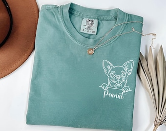 Puede incluir: Una camiseta azul turquesa con un contorno blanco de un chihuahua asomándose por la parte superior y la palabra "Peanut" debajo. La camiseta tiene una etiqueta que dice "Comfort Colors".