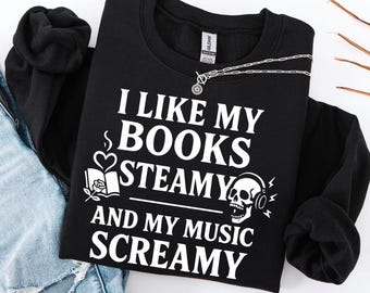 May include: Black sweatshirt with the text "I LIKE MY BOOKS STEAMY AND MY MUSIC SCREAMY" in white. The design includes a book with a heart and rose, and a skull wearing headphones. A silver necklace with a pendant is also visible.