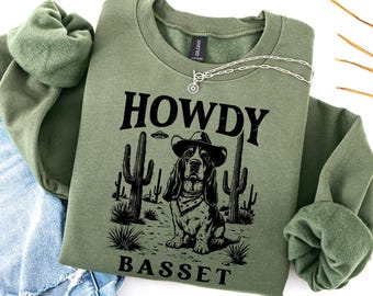 May include: Green sweatshirt with a black graphic of a basset hound wearing a cowboy hat and bandana. The text "Howdy Basset" is printed below the dog.