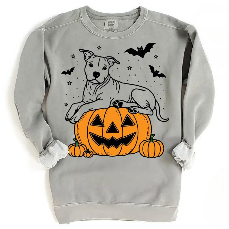 May include: A gray sweatshirt with a black and white illustration of a dog sitting on a jack-o'-lantern. The dog is wearing a collar and has a happy expression. The sweatshirt has a festive Halloween theme.