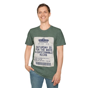 May include: Green t-shirt featuring a faux bookmaker ticket design. The ticket states "SATURDAY IS FOR THE BOYS & QUESTIONABLE ACCAS", with details including "STAKE: £10.00" and "POTENTIAL RETURNS: £268.00".