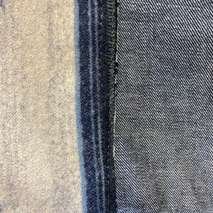 Op de afbeelding: Close-up van een denim naad met een contrasterend paneel van stof. De naad is gestikt met gele draad en de stof is een donkerblauwe denim.