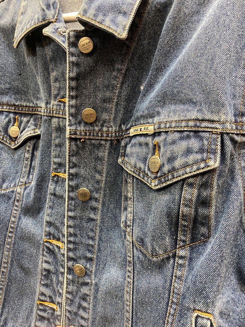 May include: A blue denim jacket with multiple silver metal buttons and a Star Blue Original label on the pocket.