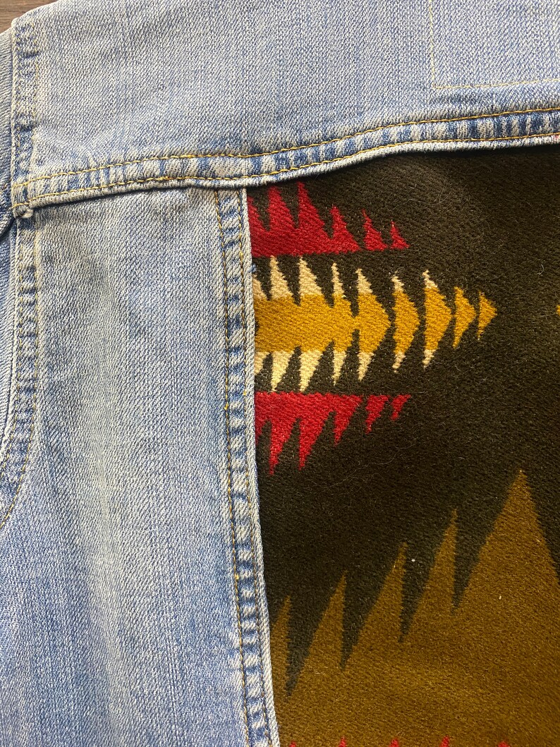 K&ouml;nnte beinhalten: Eine Jeansjacke mit einem bunten geometrischen Muster, das auf die R&uuml;ckseite gen&auml;ht ist. Das Muster besteht aus roten, gelben und schwarzen Dreiecken.