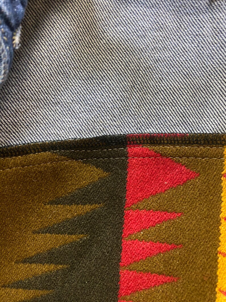 K&ouml;nnte beinhalten: Nahaufnahme einer Jeansjacke mit einem braunen, roten und gelben gemusterten Futter. Das Futter hat ein geometrisches Muster mit Dreiecken und einem dezenten Schimmer.
