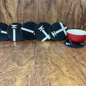 May include: Six black coasters with white geometric designs, one of which is under a red ceramic mug.