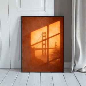 Puede incluir: Impresión enmarcada en sepia del Golden Gate Bridge en San Francisco. La silueta del puente se ve a través de una ventana, creando sombras. La impresión se muestra en una pared blanca, con una cortina visible a la derecha.