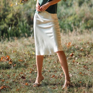 Beautiful brunette woman wearing ivory white silk slip skirt with a green silk camisole outdoors in nature. Close up