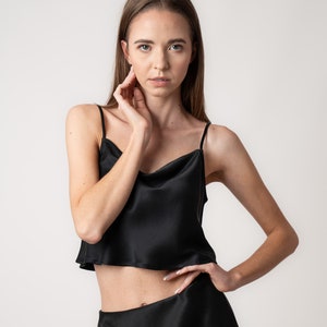 Woman wearing black silk cropped draped cowl neck camisole and black skirt in studio