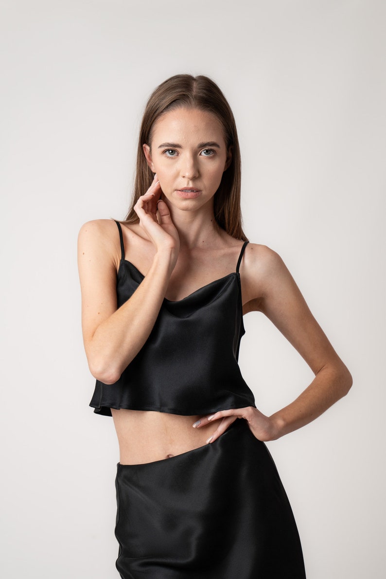 Woman wearing black silk cropped draped cowl neck camisole and black skirt in studio