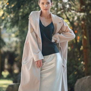 Beautiful brunette woman wearing ivory white silk slip skirt with a black silk camisole outdoors in nature. Hair tied up. Wearing cream long jacket