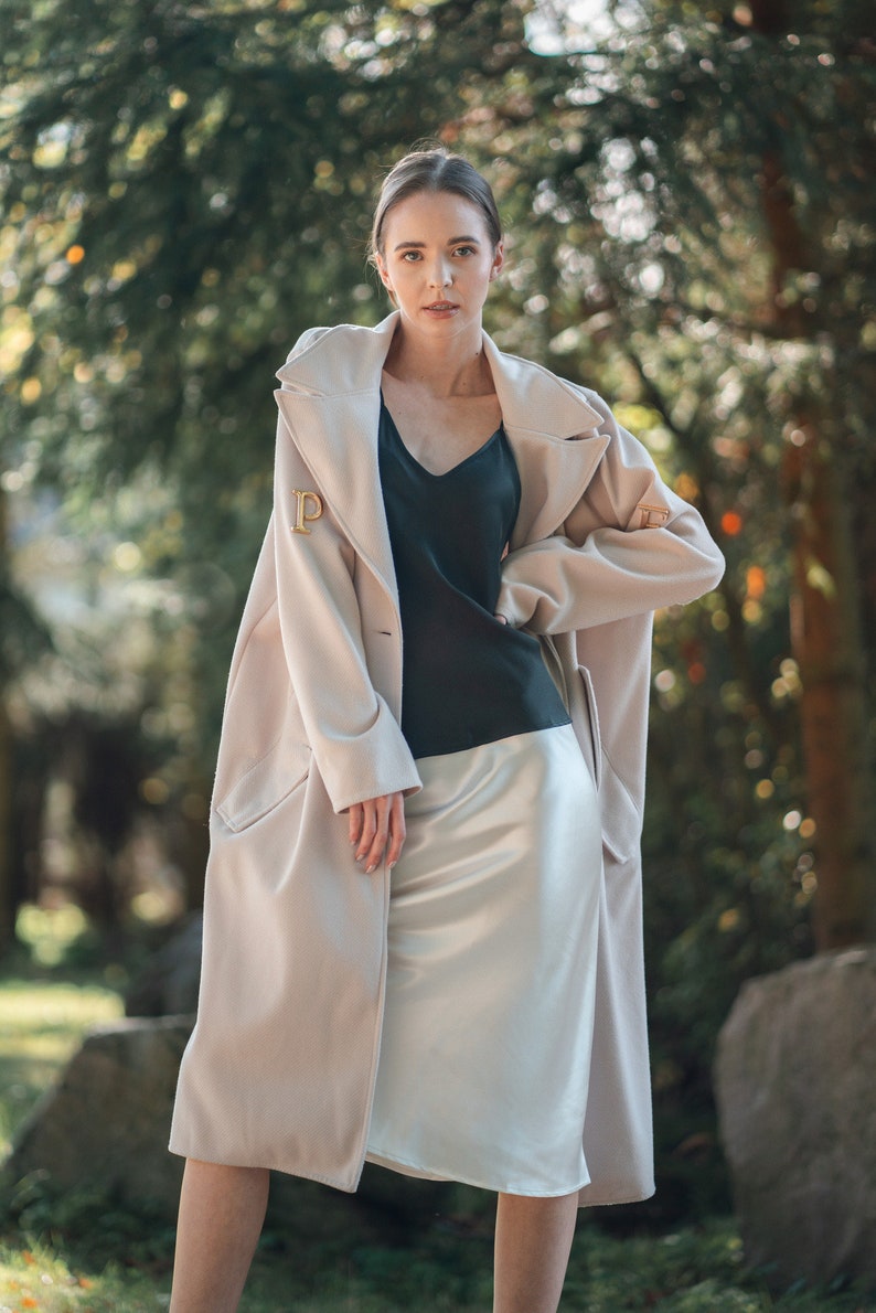 Beautiful brunette woman wearing ivory white silk slip skirt with a black silk camisole outdoors in nature. Hair tied up. Wearing cream long jacket